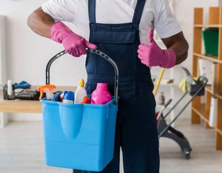 Cropped view of African american cleaner showing thumb up and holding bucket of detergents in office